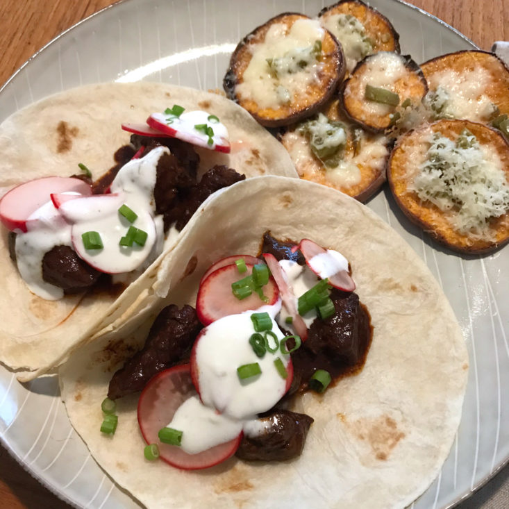close up of completed ancho beef tacos and cheesy sweet potato with pickled jalapeno and lime sour cream on plate