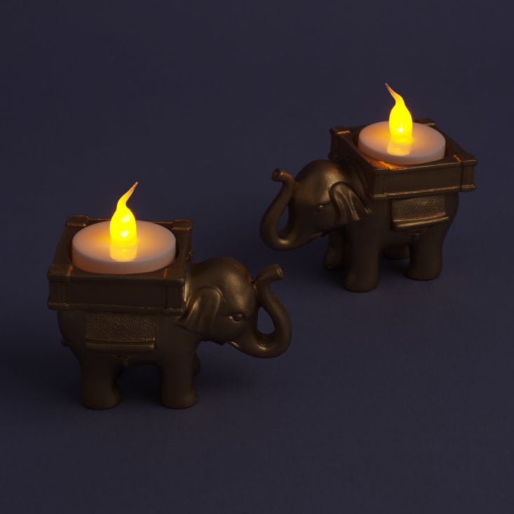 a pair of elephant votive candle holders with battery operated tea lights in them, glowing in the dark