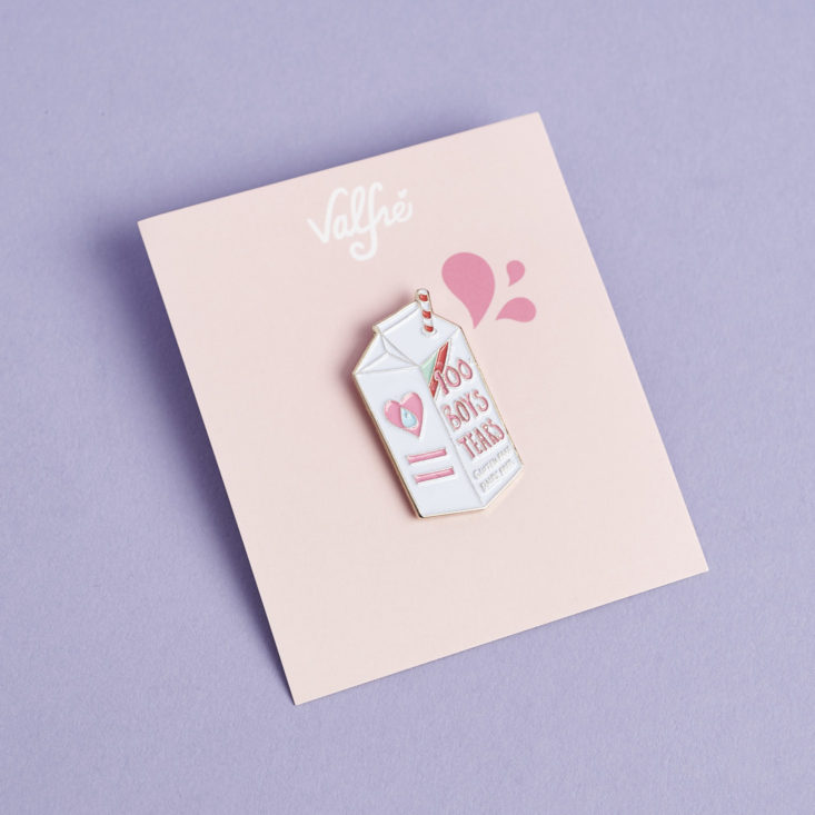 a white milk carton shaped enamel pin that says "100% boys tears" in pink on it in its pink valfre packaging