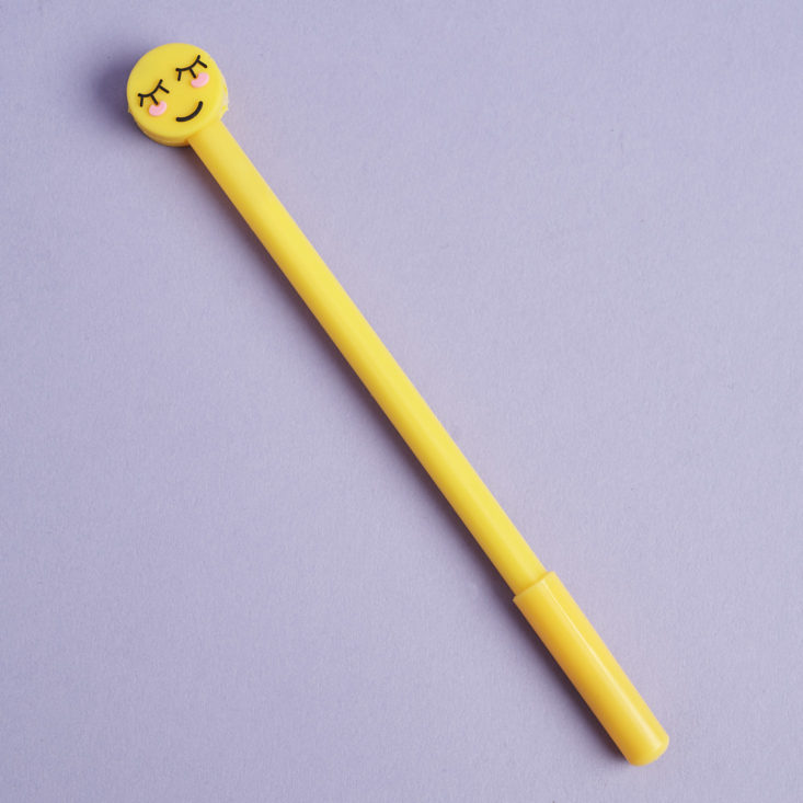 a yellow pen with black ink and a blushing emoji topper